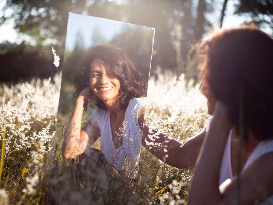 woman sitting in a field looking at self in mirror